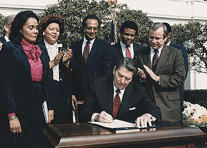 On November 2, 1983, President Ronald Reagan signs legislation creating a national holiday in honor of Martin Luther King as Coretta Scott King (left) looks on.Photo via NewsCom